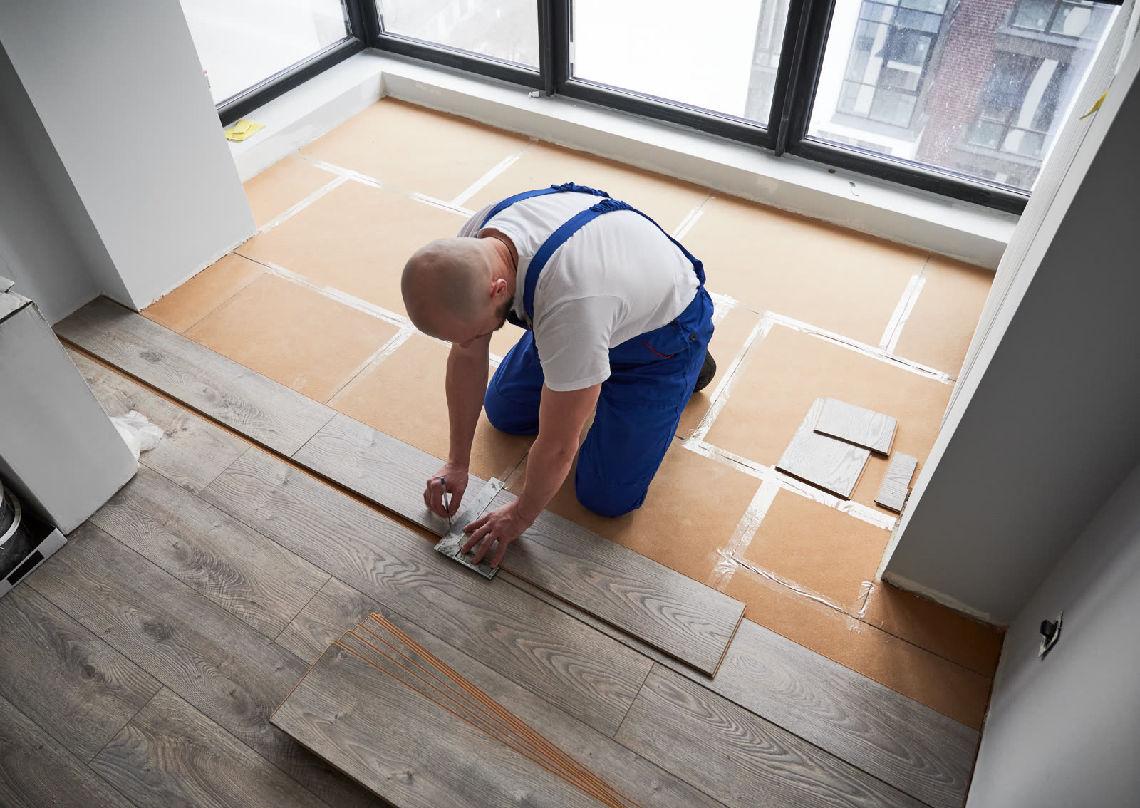 Male worker measuring and marking laminate plank i — the kind of handyman work vetted local pros handle in Sarasota, FL