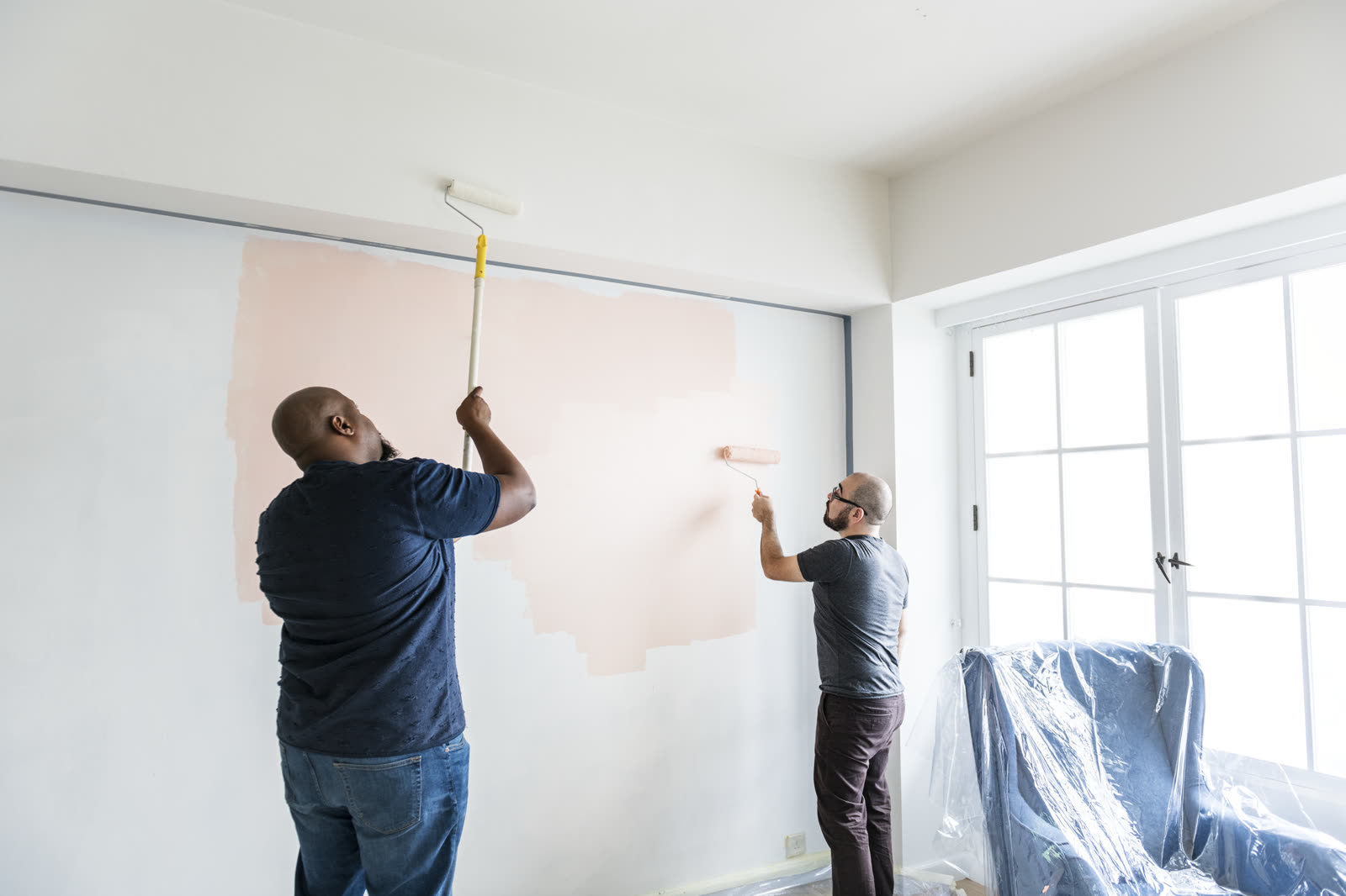 Two painters rolling a new color onto an interior living room wall